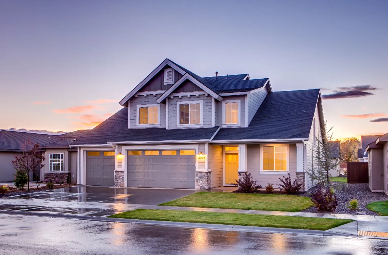 Gray two-story home with an attached garage and lit windows at dusk
