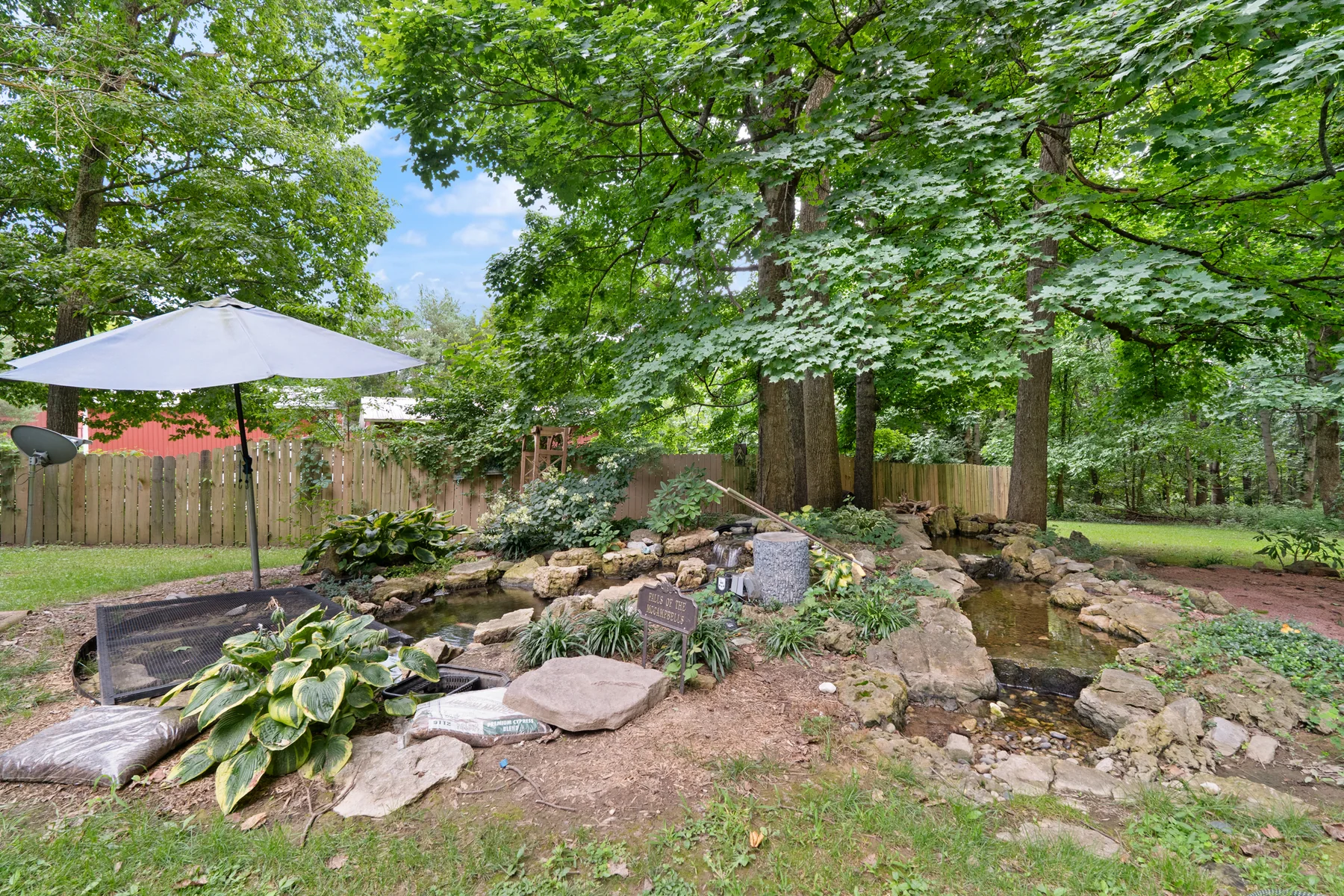 Landscaped koi pond with waterfall beneath mature shade trees