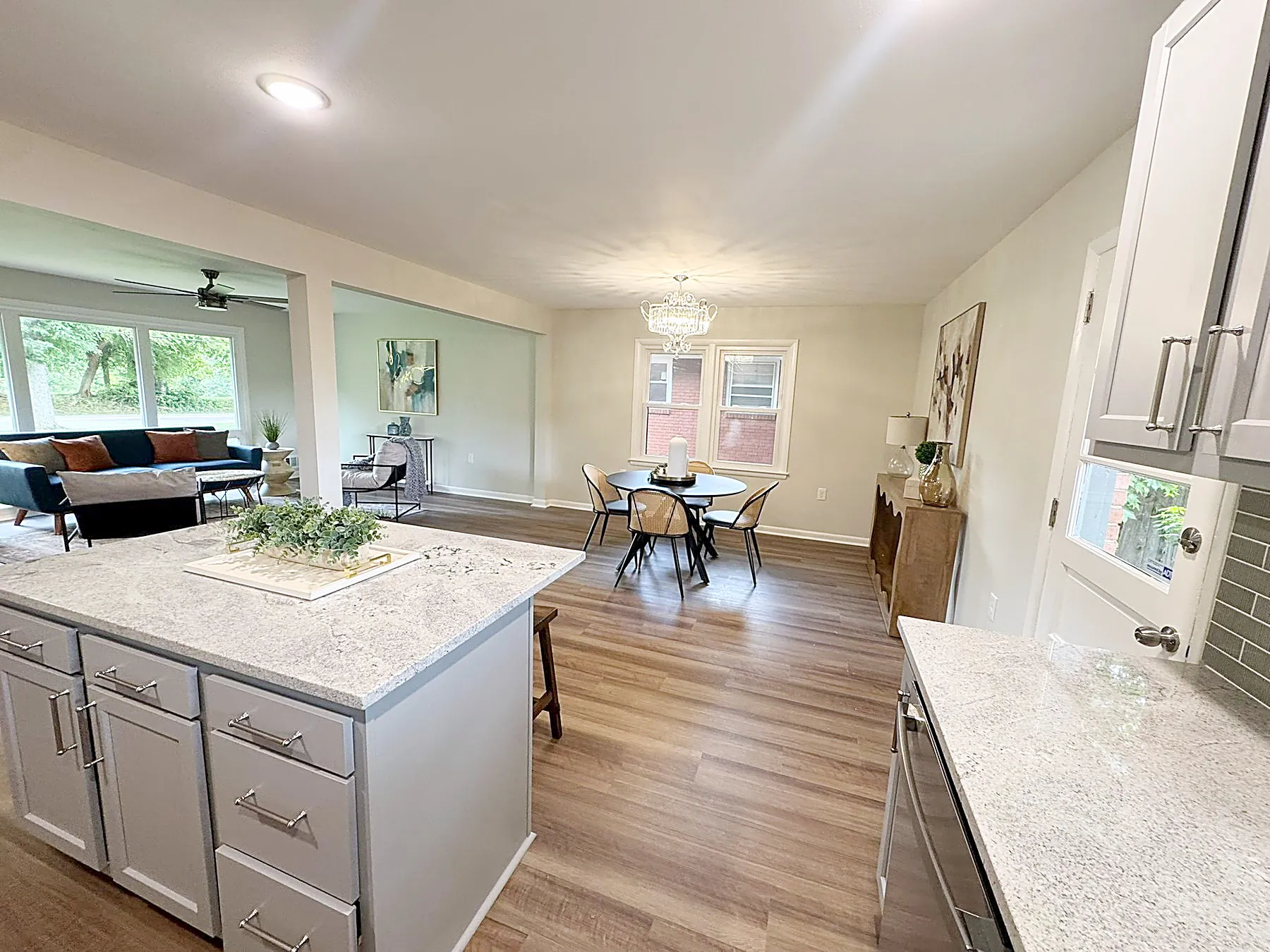 Open kitchen with granite countertops, a large center island, tile backsplash, and stainless appliances flowing into the living and dining areas