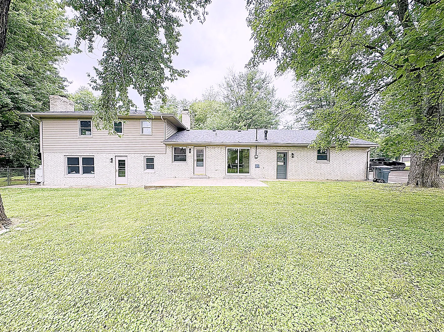 Wide rear yard with mature shade trees and an expanse of green lawn
