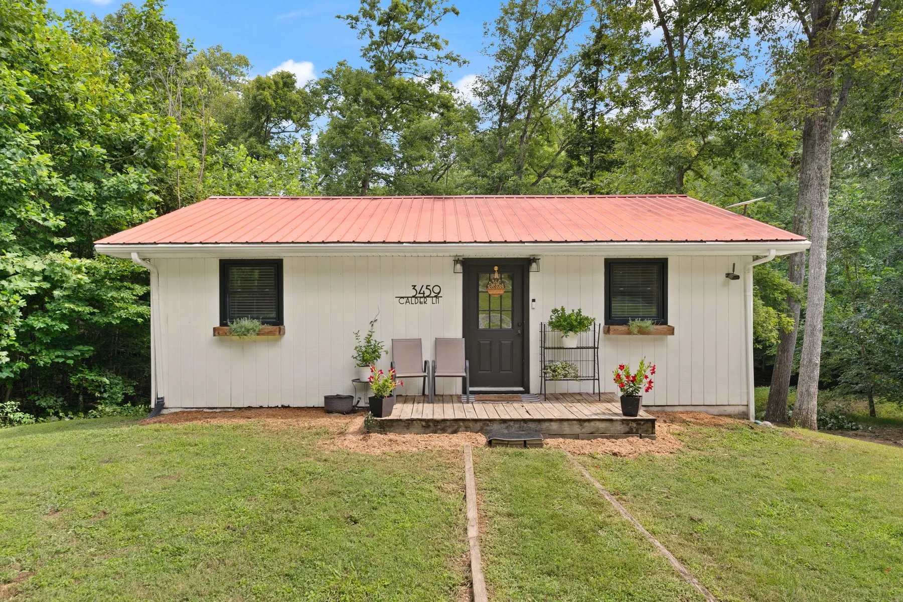 Front elevation: white board-and-batten cottage with a rust standing-seam metal roof and cedar window boxes