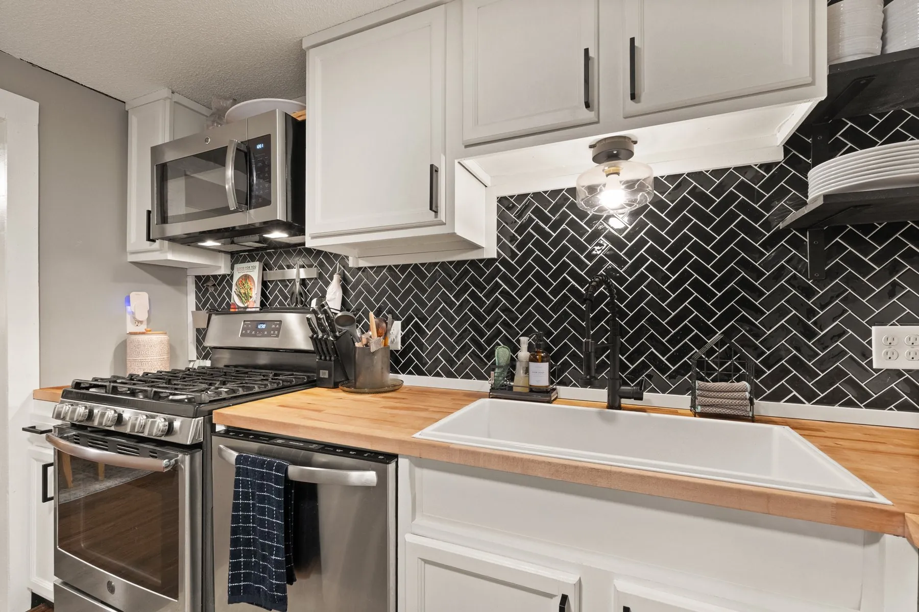 Kitchen with white shaker cabinets, butcher-block counters and a black herringbone tile backsplash