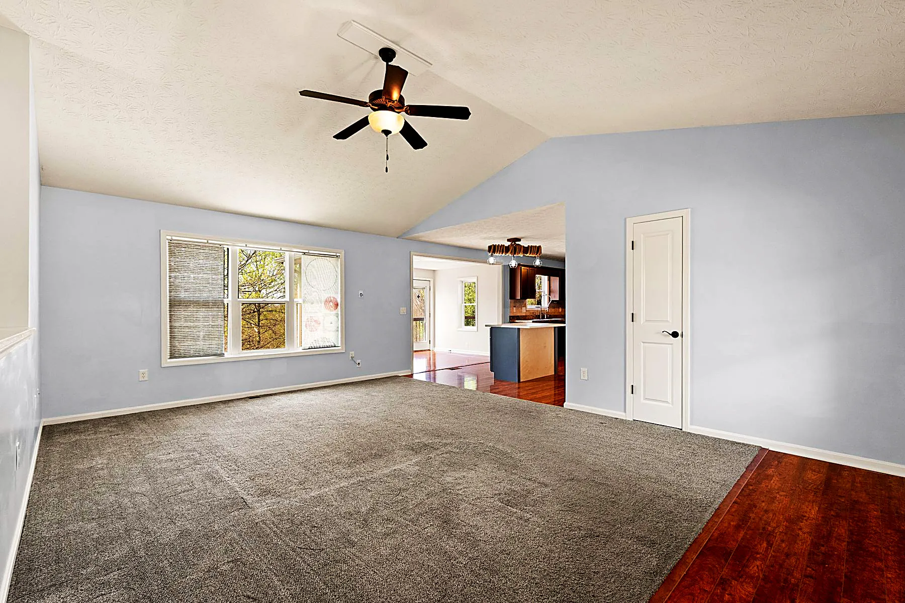 Great room with a vaulted ceiling and large windows looking out to the wooded lot