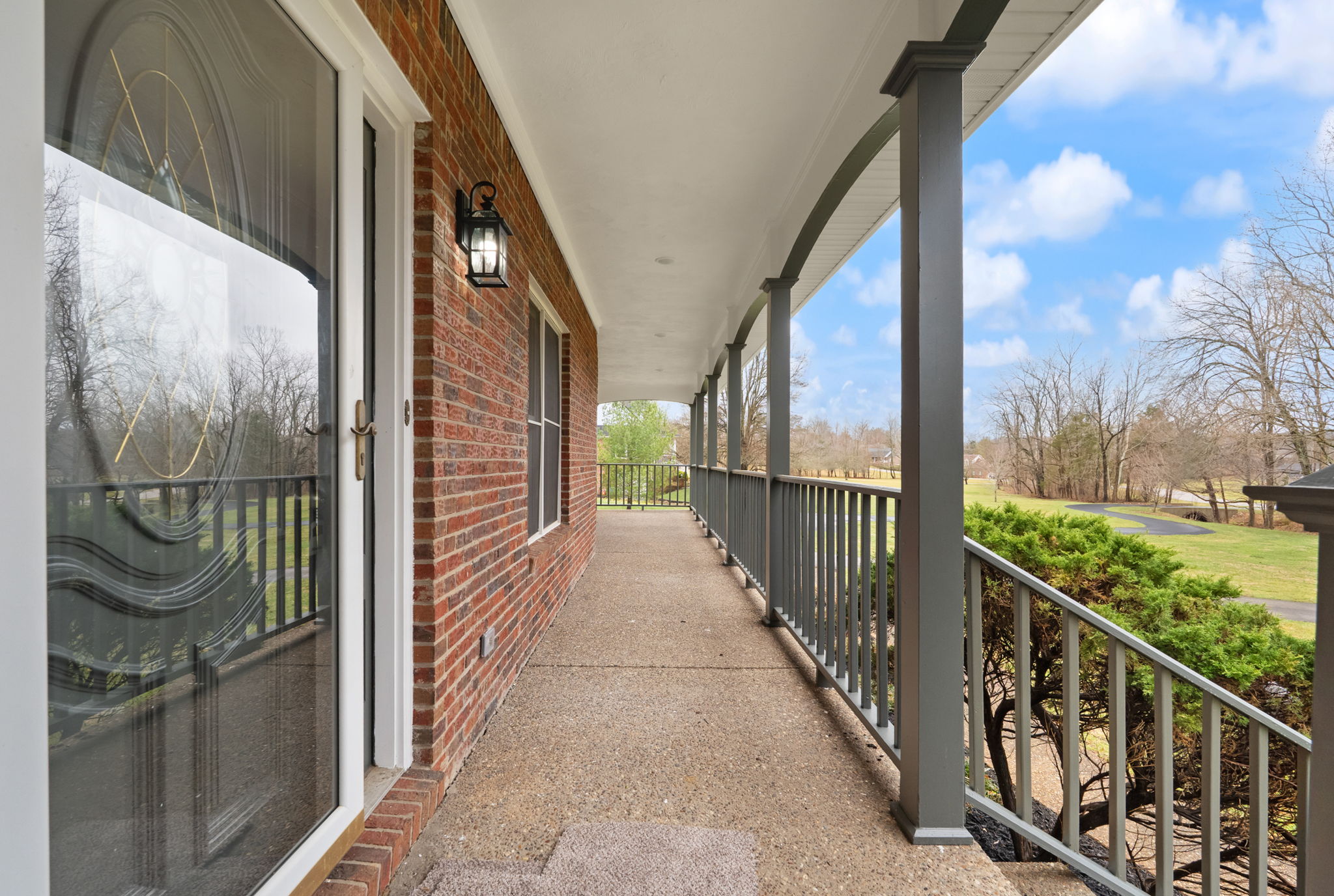 Covered wraparound porch with columns, view of lawn and trees