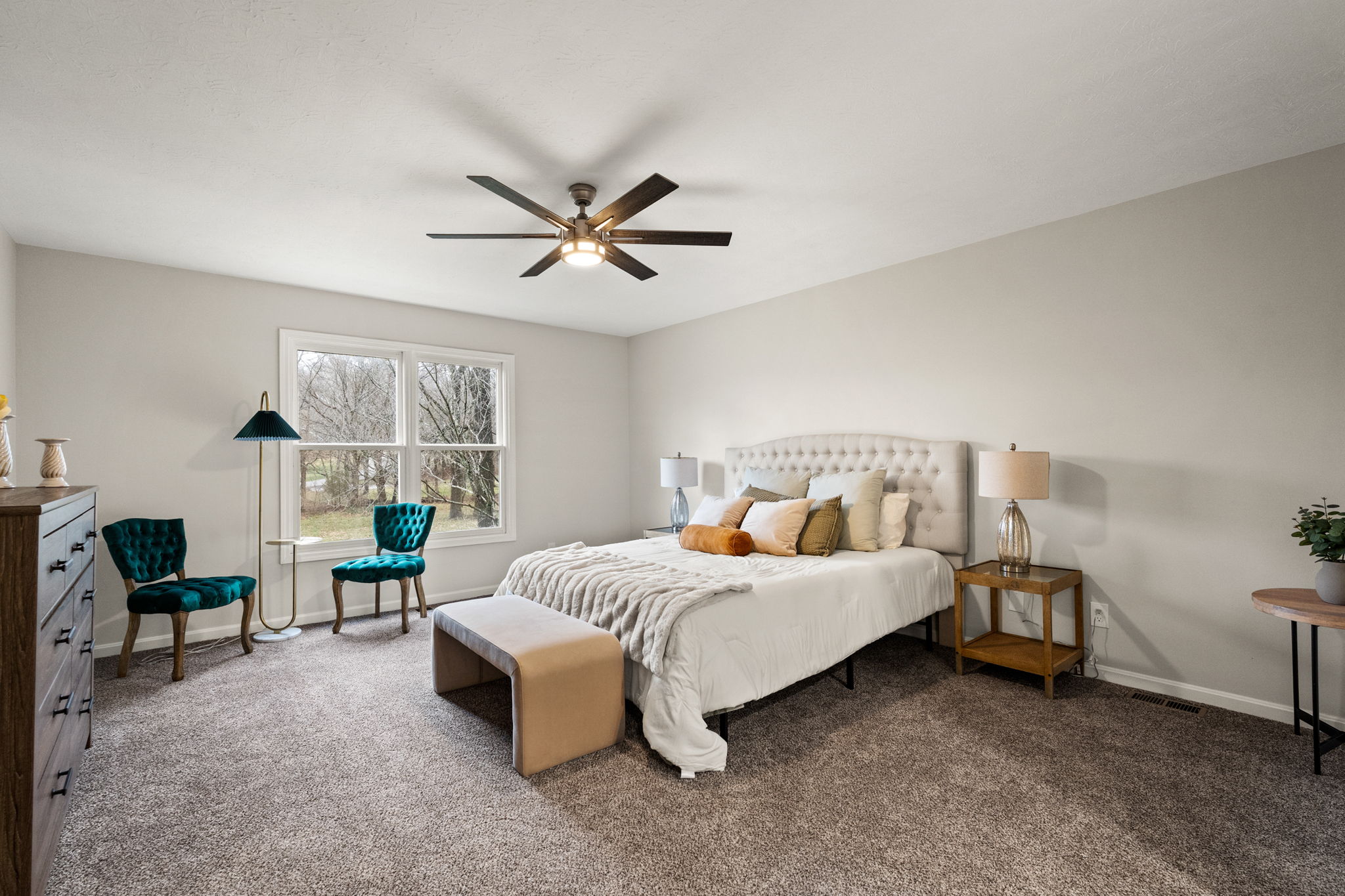 Primary bedroom with white tufted headboard, teal accent chairs, and ceiling fan