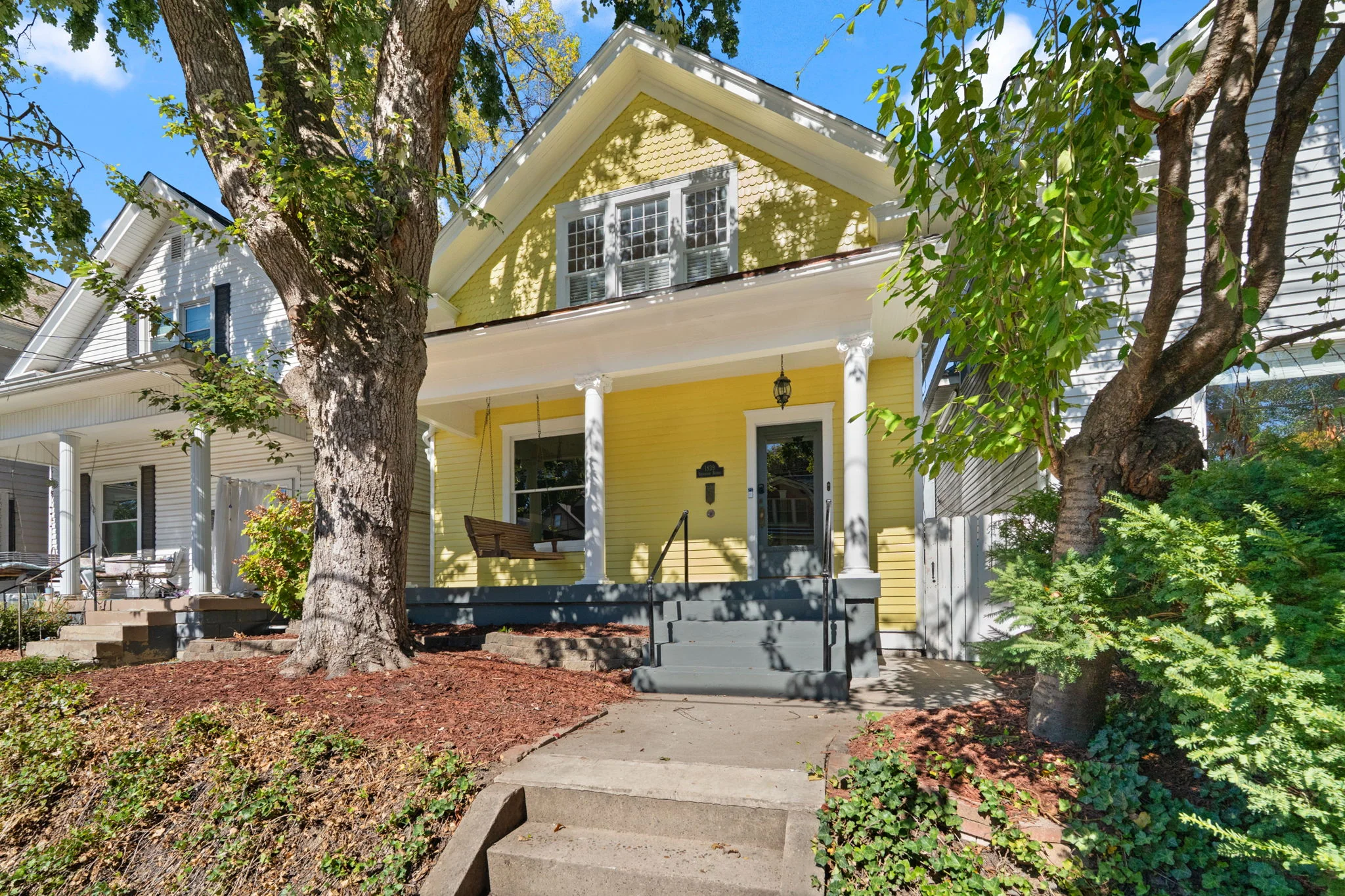 The covered front porch and yellow exterior, framed by mature trees. 1839 Sherwood Avenue, Louisville, Kentucky.